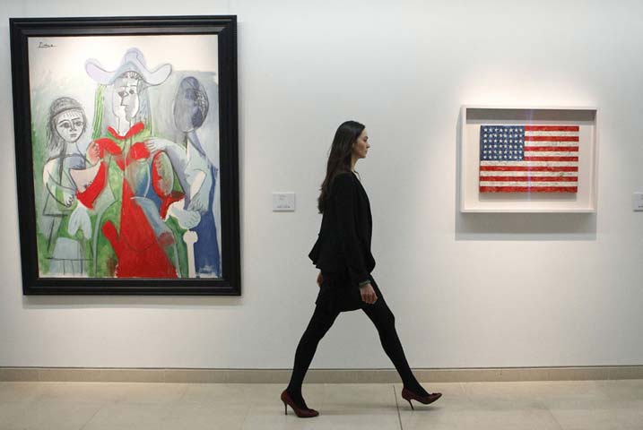 Cô Laura Vere-Hodge của nhà Christie’s đi ngang bức tường treo tranh một gallery có hai bức: "Femme et Fillettes" của Picasso và "Flag" của Jasper Johns, tại một cuộc đấu giá ở London hồi 5. 2. 2010